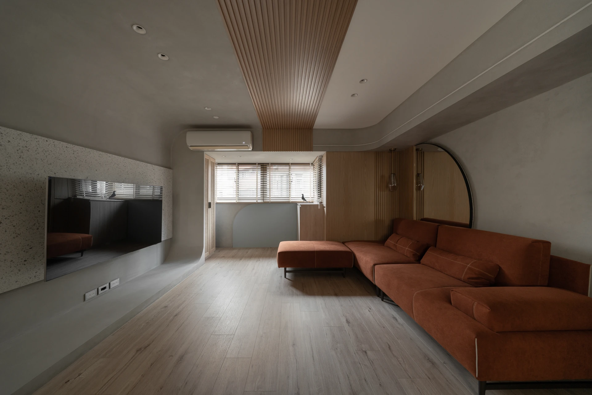 新竹舊屋翻新客廳，磚橘絨布沙發與磨石子拱形電視牆、圓鏡與木格柵天花 — 覺壹設計